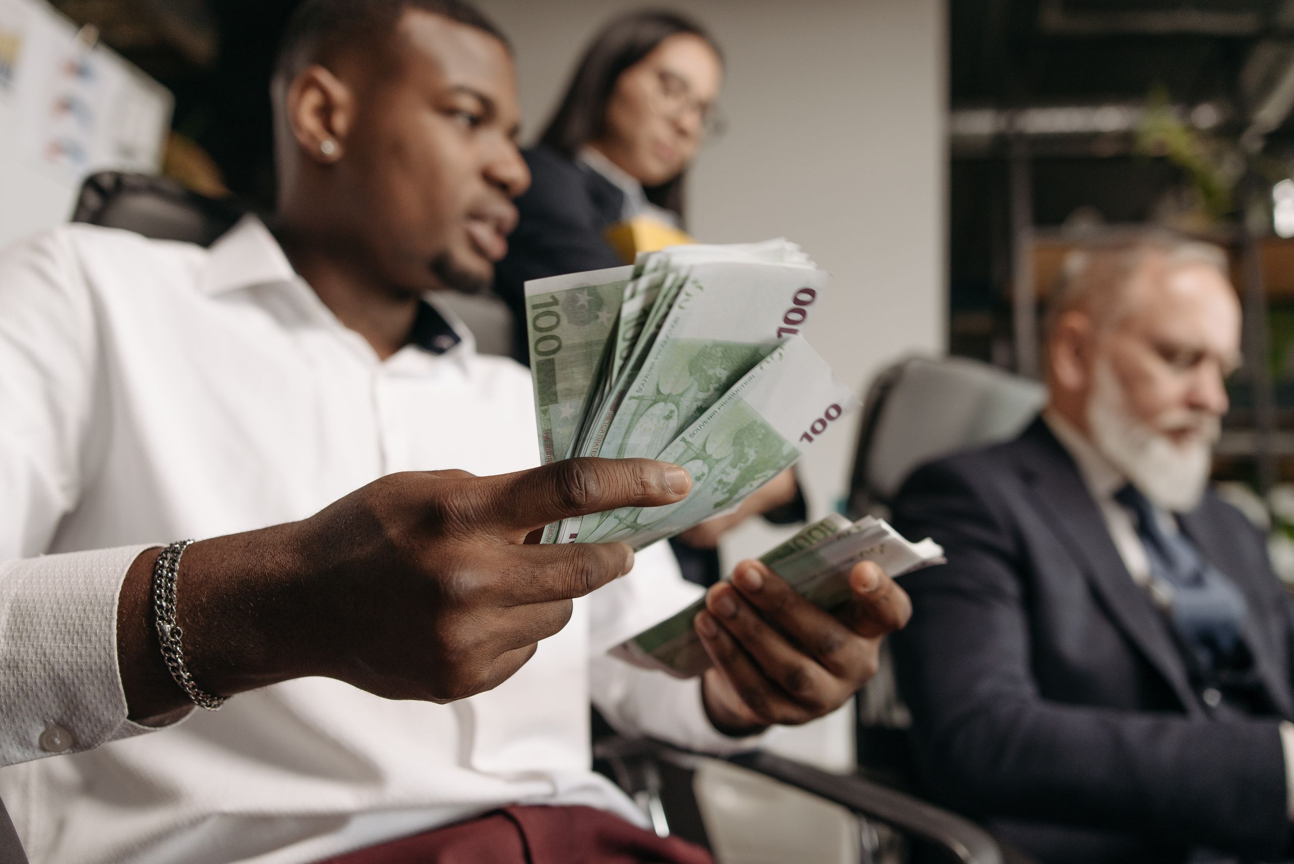 Jobber Financing: How It Works, Benefits, Costs & Financing Options for Contractors 1 Three professionals in business attire counting cash in a modern office setting.
